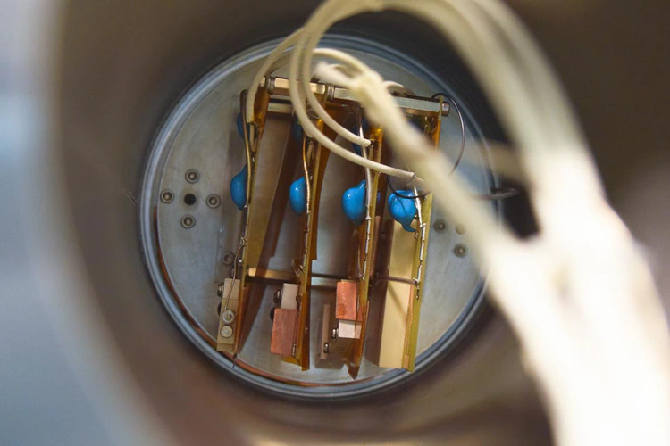 Four parallel PCBs placed on a metal disk. Standoffs between the PCBs provide spacing. White wires routed to each originating in the foreground. Two blue capacitors on mounted on each PCB.